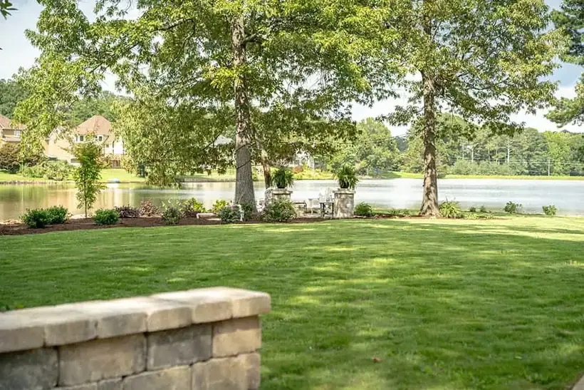 Lakeside lawn and stone seat wall under shade trees